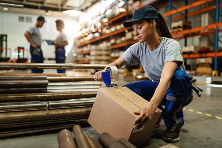 Young woman working in warehouse and taping cardboard box for shipment